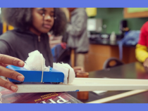 African-American female student doing experiment with toy car on plank